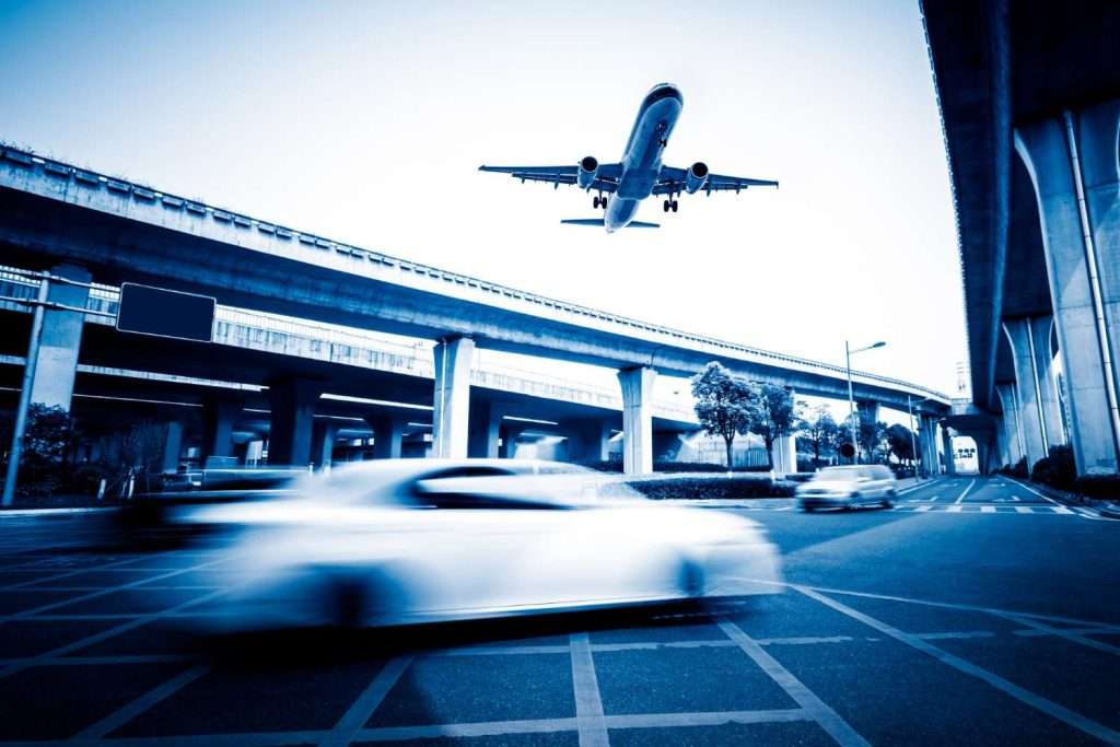 VTC Elvis Avión aterrizando sobre una calle urbana muy transitada con coches borrosos en movimiento bajo autopistas elevadas, que recuerdan a los tours turísticos en Cantabria en un tinte azul. servicios de VTC en Cantabria