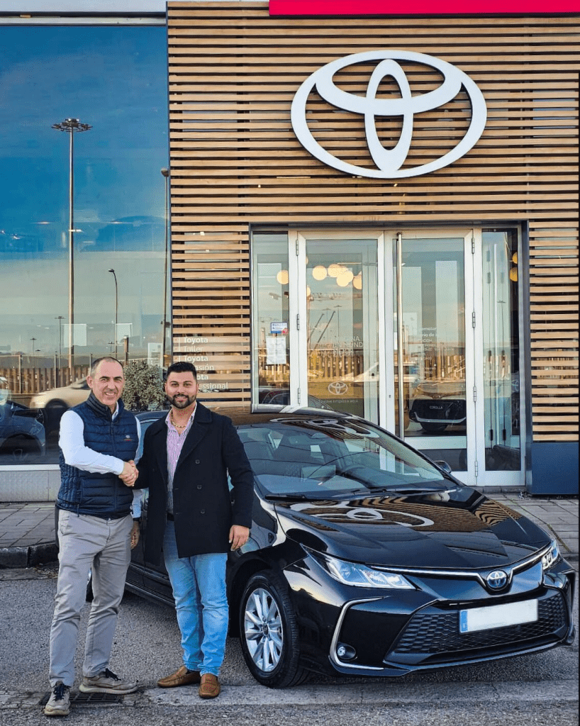 VTC Elvis Dos hombres se dan la mano junto a un coche negro en un concesionario de Toyota, listos para realizar tours turísticos en Cantabria. servicios de VTC en Cantabria