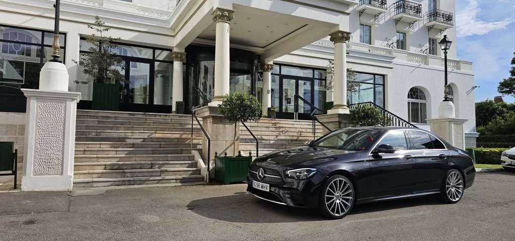 VTC Elvis Un coche de lujo negro, ideal para transporte de eventos privados en Cantabria, está aparcado delante de un gran edificio blanco con elegantes escaleras y columnas. servicios de VTC en Cantabria