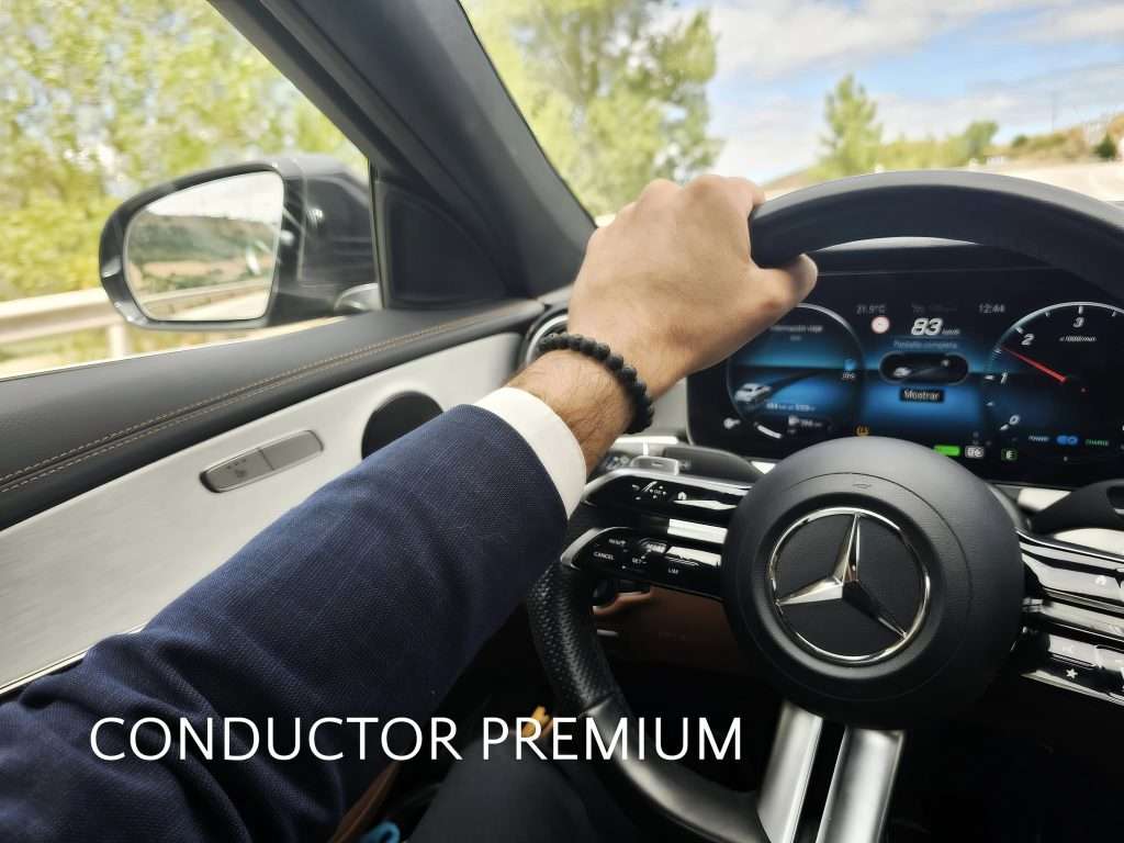 VTC Elvis Primer plano de la mano izquierda de una persona en el volante de un Mercedes-Benz, con la carretera y los frondosos árboles desplegándose a través del parabrisas, ofreciendo una visión de la serena experiencia del transporte ejecutivo en Cantabria. servicios de VTC en Cantabria