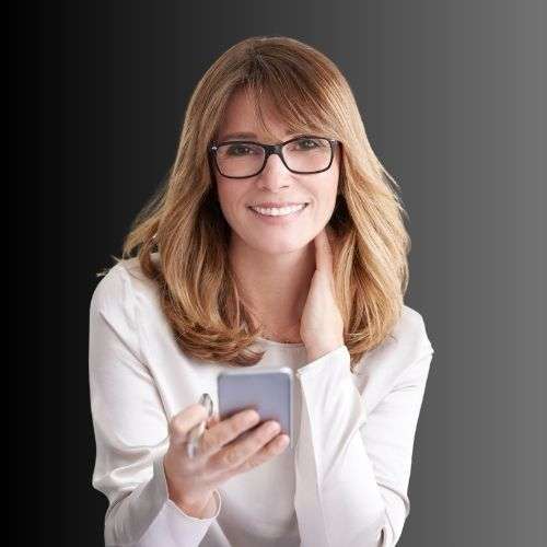 VTC Elvis Una mujer con gafas sonríe mientras sostiene un teléfono inteligente, vistiendo una blusa blanca sobre un fondo degradado oscuro. servicios de VTC en Cantabria