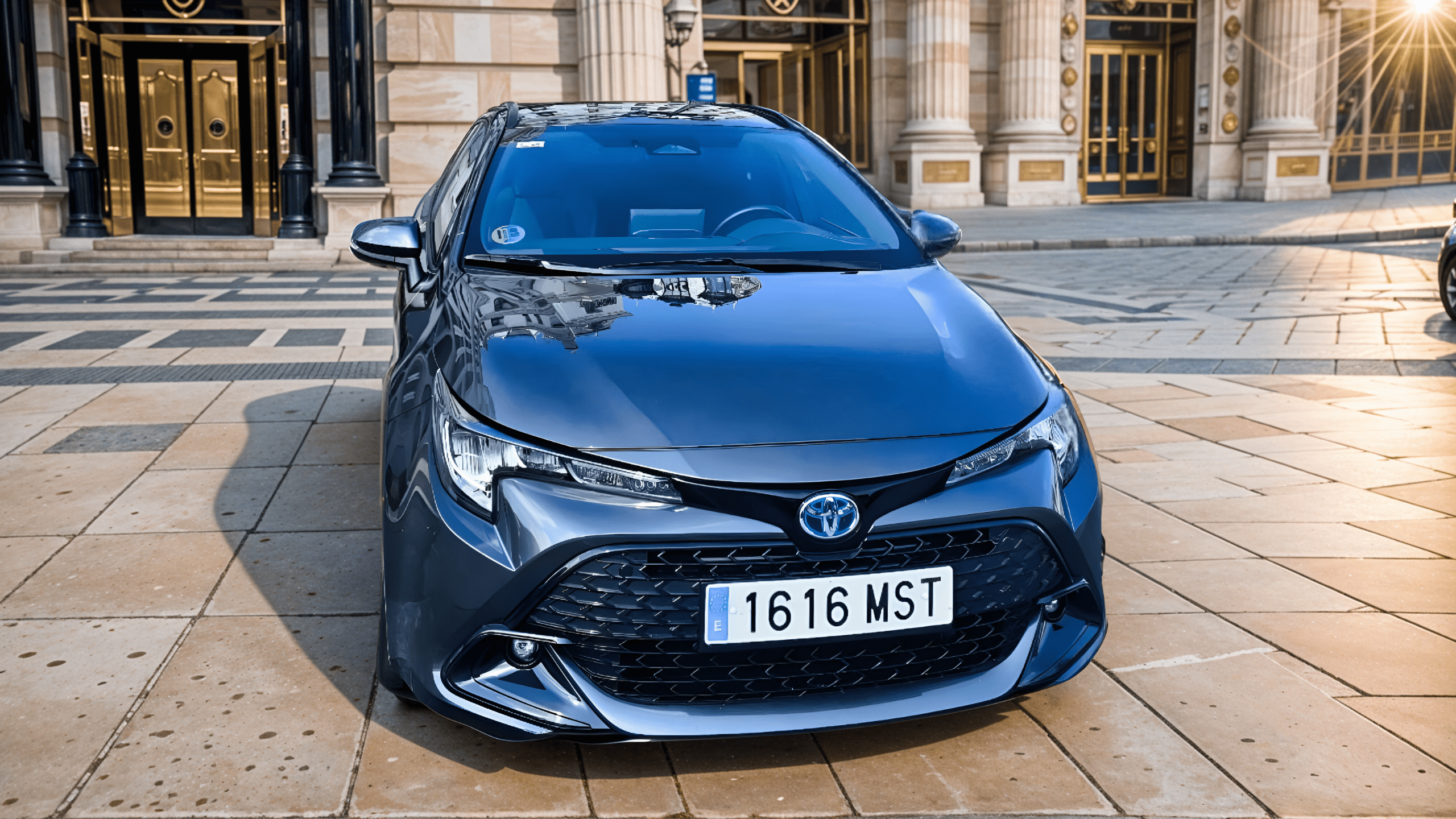 VTC Elvis Un automóvil Toyota azul, parte de la flota de vehículos VTC en Cantabria, está aparcado en una calle adoquinada frente a un edificio ornamentado con puertas altas. servicios de VTC en Cantabria