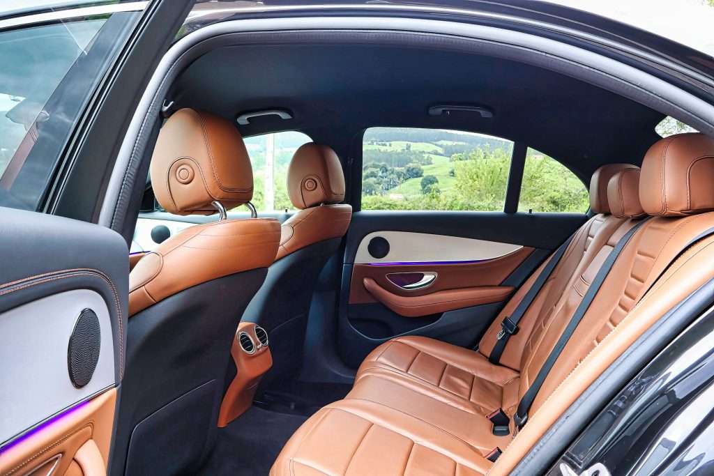 VTC Elvis Interior de coche de lujo con asientos de cuero color canela, una puerta abierta que ofrece una vista de exuberante vegetación a través de las ventanas, que recuerda a un vehículo premium de una flota de vehículos VTC en Cantabria. servicios de VTC en Cantabria