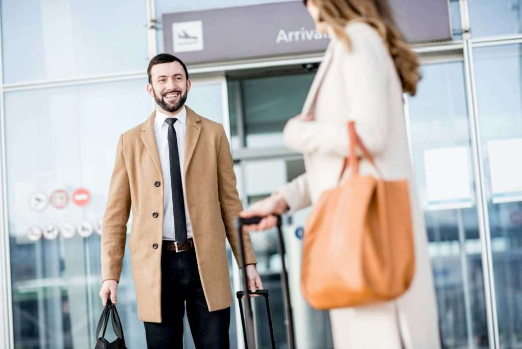 VTC Elvis Un hombre con una maleta sonríe a una mujer con un bolso en la zona de llegadas del aeropuerto. servicios de VTC en Cantabria
