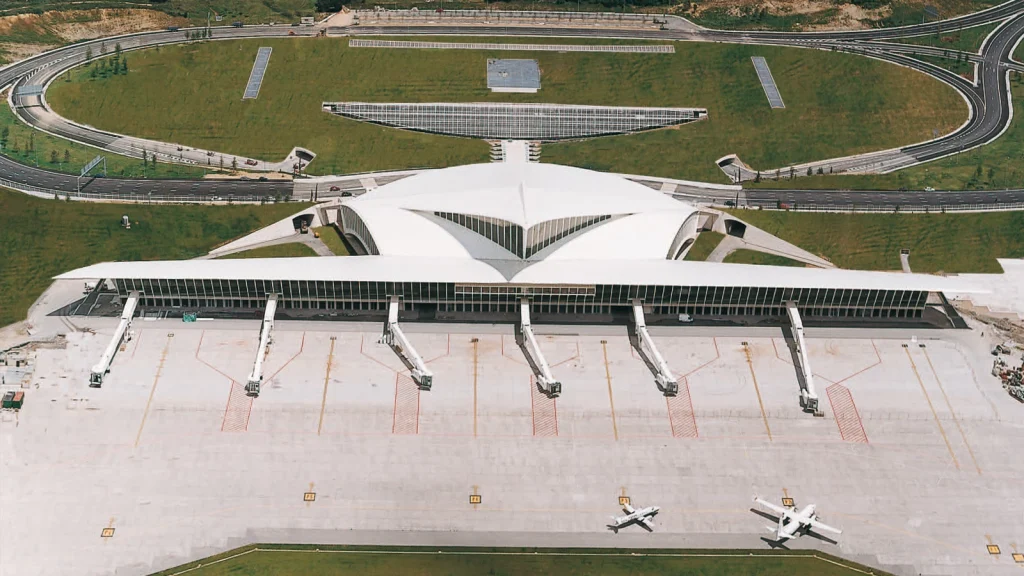 VTC Elvis Vista aérea de una moderna terminal de aeropuerto con pasarelas de embarque, zonas verdes y aviones en la pista, ideal para traslados al aeropuerto de Bilbao. servicios de VTC en Cantabria